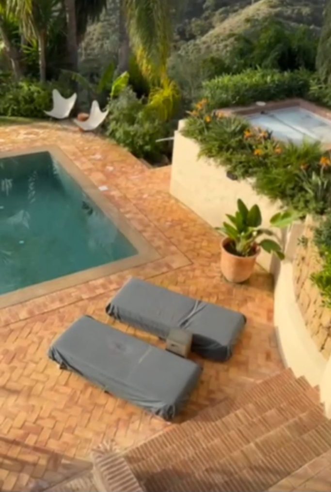 Proyecto con ladrillo tosco envejecido Zona de piscina con tumbonas grises y plantas, rodeada de vegetación.